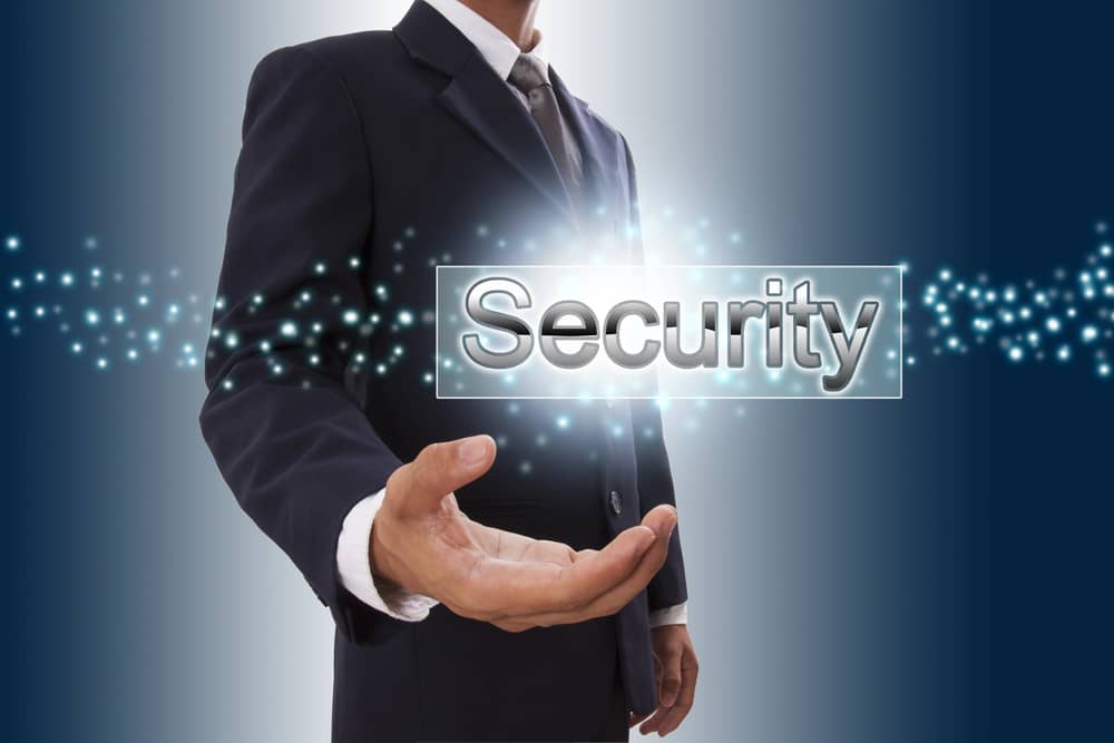 Un hombre de negocios presenta la palabra "Security" (Seguridad) en su mano abierta, sobre un fondo con un efecto de partículas brillantes.