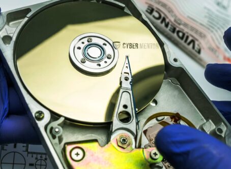 Manos en guantes azules examinando un disco duro abierto.