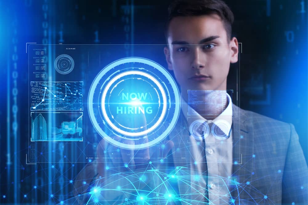 Un hombre en traje interactúa con una interfaz digital que muestra el mensaje "NOW HIRING", indicando oportunidades de trabajo en el campo de la ciberseguridad.