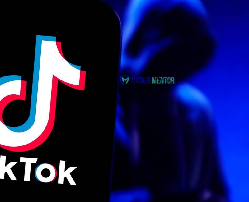 El logo de TikTok en una pantalla de teléfono inteligente, con una figura encapuchada y difuminada al fondo, sugiriendo un contexto de cibercrimen. El logo de Cyber Mentor también está presente.