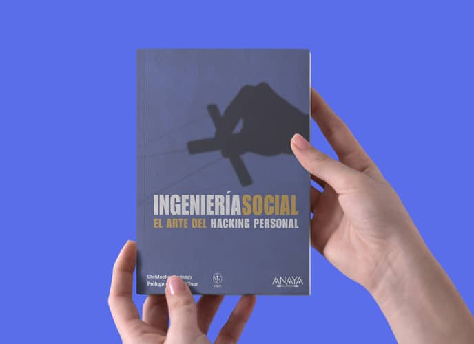 Unas manos sujetan la portada de un libro titulado "Ingeniería Social: El arte del hacking personal", con un fondo azul.