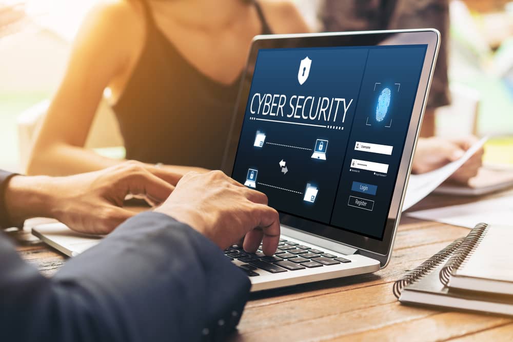 Cursos de ciberseguridad: personas trabajando en portátil con interfaz "Cyber Security", promoviendo formación y protección de datos.
