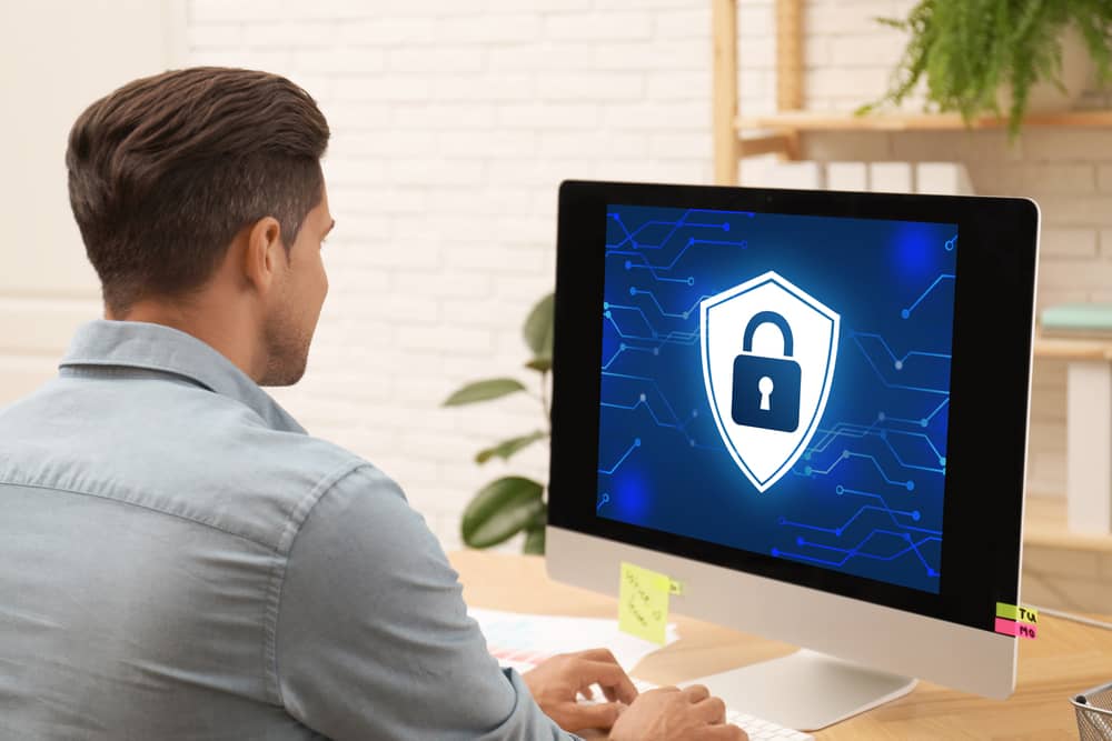 Formación en ciberseguridad para empresas: hombre trabajando en ordenador, con icono de candado y escudo en pantalla, promoviendo la seguridad de datos.